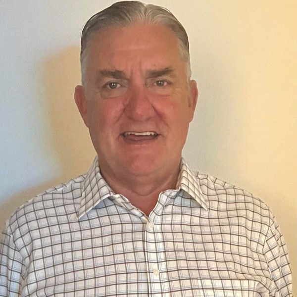 A man in a checkered shirt standing in front of a wall.