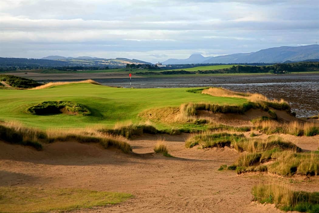 A Golf Course With Sand Dunes And Water In The Background.