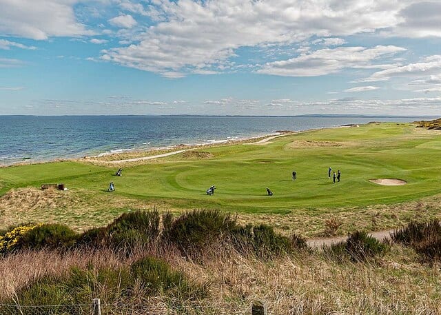 A Group Of People Playing Golf On A Hill Overlooking The Ocean.