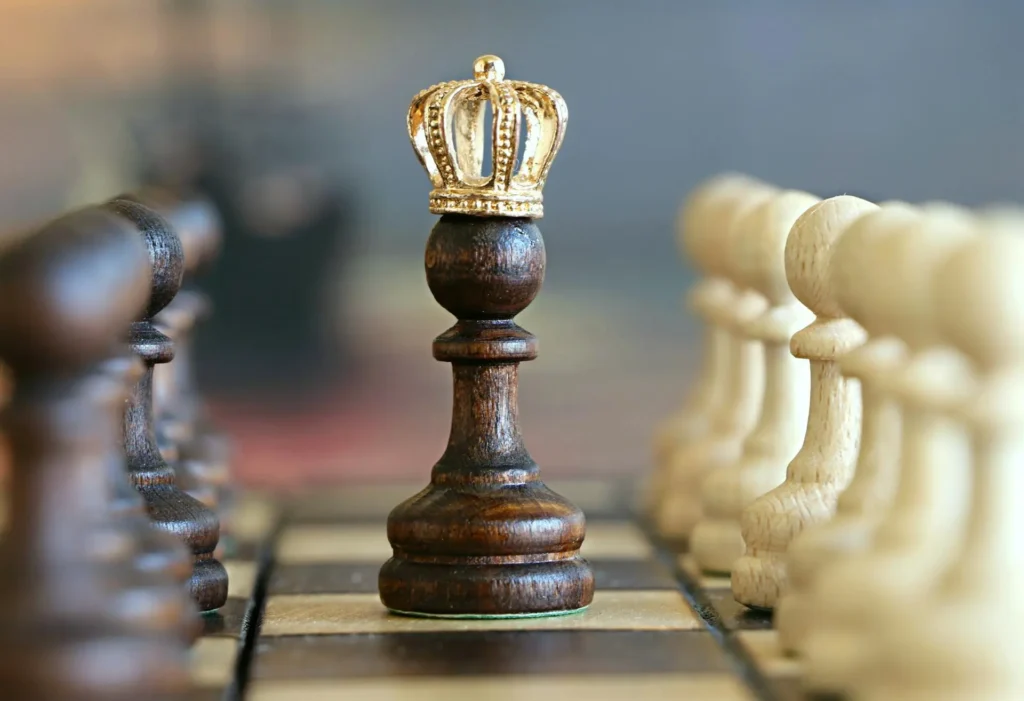 A Chess King Piece With A Crown, Standing On A Board Between Rows Of Blurred Black And White Chess Pieces, Evoking The Controversial History Of Figures Like Mary Queen Of Scots.